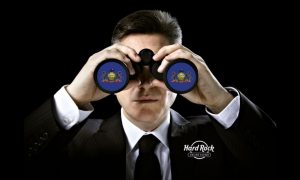 Man looking through binoculars that are focused on the Pennsylvania state flag. He has a Hard Rock online casino logo on his suit. The online casino market has been booming as of late, especially in the Pennsylvania market. Several new operators have entered the Keystone State since 2022 and have found success. Industry expert and the author of Straight To The Point newsletter, Steve Ruddock, believes another prominent online casino operator is primed for expansion and should target the PA online casino market. Hard Rock could be next to expand to the Keystone State Hard Rock Digital is one of the more well-known entertainment establishments with a presence both in the retail and online vertical. The company recently bought the assets of Sports Illustrated’s online brand, 888, according to a press release. Sports Illustrated had been operating in Michigan for about a year. The move by Hard Rock is a clear indication the operator plans to expand its online footprint. Ruddock mentioned the Keystone State as a destination for Hard Rock. He said in his newsletter on Thursday: “After the conclusion of its ‘strategic review,’ 888 announced that it is selling its US B2C business to Hard Rock Digital, giving the latter a pathway into the online casino states of Pennsylvania and Michigan.” Hard Rock isn’t too far from Pennsylvania to begin with. It launched an online casino in neighboring state New Jersey in August 2023. It also has an online sportsbook in the Garden State and in Florida, too, which went live earlier this year as the only platform. Pennsylvania does not have a limit on the number of casino operators that can join the state. Since Hard Rock does not have a retail location in the Keystone State, it would have to partner with another land-based option or enter as a Qualified Gaming Entity (QGE). Newest Keystone State online casinos finding success Since the start of 2022, there have been five online casino operators joining the Pennsylvania market. Those include: Tropicana Casino Golden Nugget Bally's Jackpot City Fanatics Casino Each of these operators have experienced success, albeit at varying degrees. Tropicana is another Caesars skin, partnered with Harrah’s Philadelphia, and produced $10 million or more in revenue in two of the last three months. Harrah’s Philadelphia is becoming a top licensee within the state. Since launching in late August, Golden Nugget has amassed more than $32 million in lifetime earnings, averaging $4.6 million in monthly revenue. Having merged with DraftKings in 2022, Golden Nugget figures to be a strong operator for the foreseeable future. Bally’s went live in Pennsylvania just before Golden Nugget did. The operator reported its best months ever in January and February, recording $3.4 million and $3.9 million, respectively. Fanatics, partnering with Hollywood Penn National, helped the licensee jump nearly 30% in month-over-month revenue in February. The new operator already has significant brand awareness for its merchandise and expects to further improve its gambling stature. If all of the above operators are able to succeed, there’s no reason why Hard Rock can’t, and shouldn’t be looking to enter the Pennsylvania market.
