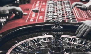 Black and red image of a roulette table with a dealer's hand on on the wheel about to spin. Dealer Robin Schnepp, and supervisor Anthony Laush are accused of helping at least two players cheat at roulette to the tune of $10,000.