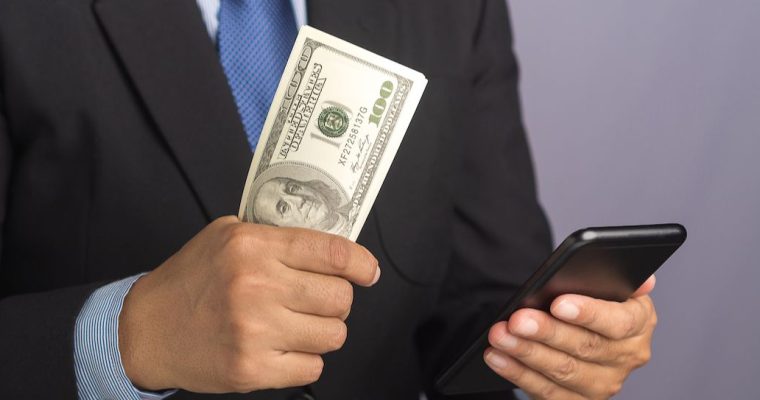 Businessman holding US cash and a phone. The PGCB fined Live! Casino Philadelphia $100,000 on Wednesday for violating the proxy wagering rule at the casino's retail sportsbook.