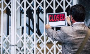 Closed metal gate over the front of a business and a person hanging a "closed" sign on the door. Betway has decided to close up sports betting operations in Pennsylvania, but will continue to offer its online casino product.
