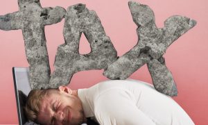 Businessman with his head on a laptop keyboard as the large word "TAX" is pressing down on his head and back. In response to states raising sports betting taxes, DraftKings has made a controversial decision to slap PA sports bettors with a surcharge.
